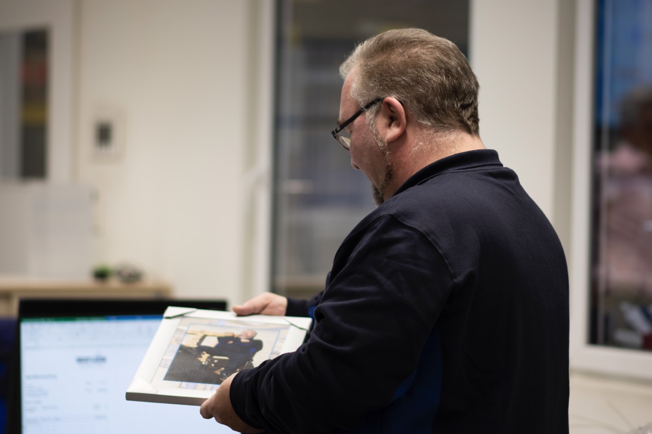 Mann steht in einem Büro und schaut auf einen Bilderrahmen. 